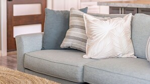Ein Wohnzimmer mit grauem Sofa, einem gewebten Hocker und einer Holztür mit Milchglas-Fenstern.