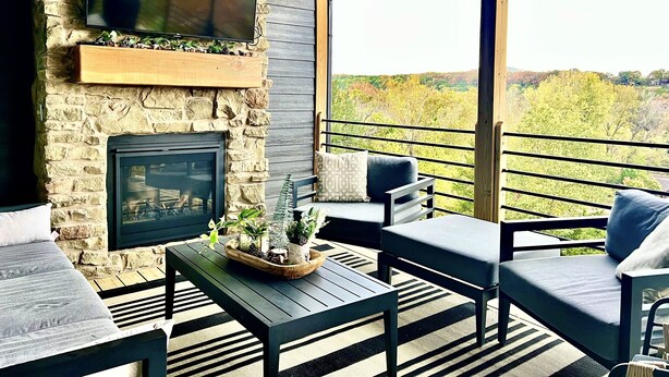 A cozy outdoor seating area with a stone fireplace, a flat-screen TV, and a view of the surrounding landscape. - Luxury at Lake Taneycomo, Hot Tub, FirePit, Views! (Hollister)