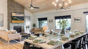 A spacious dining area with a long table set for a meal, surrounded by chairs, in a room with wooden ceilings and stone walls. - Luxury at Lake Taneycomo, Hot Tub, FirePit, Views! (Hollister)