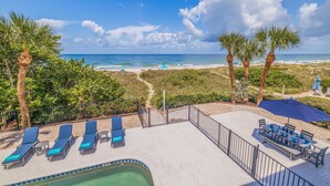 A pool area with lounge chairs, a dining table, and a view of the beach and ocean. - Casa Al Mare 101 – Beachfront Luxury w/ Saltwater Pool, Private Trail, Balconies & Sunset Views (Indian Rocks Beach)