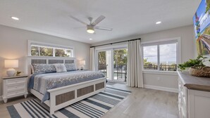 A bedroom with a bed, nightstands, a ceiling fan, and a view of the outdoors through large windows. - Casa Al Mare 101 – Beachfront Luxury w/ Saltwater Pool, Private Trail, Balconies & Sunset Views (Indian Rocks Beach)