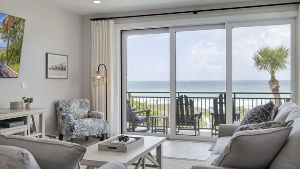 A spacious living room with a large sliding glass door leading to a balcony with a view of the ocean.