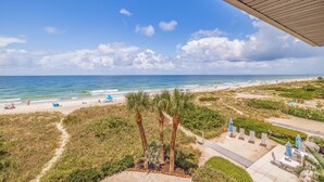 A beach view with a pathway leading to a seating area with umbrellas.