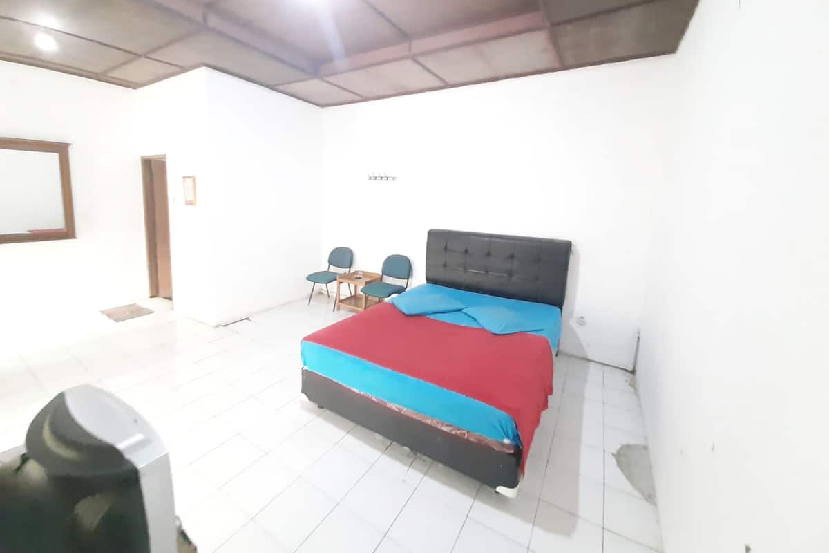 Ein Schlafzimmer mit einem Bett, zwei Stühlen, einem kleinen Tisch und einer Deckenleuchte.