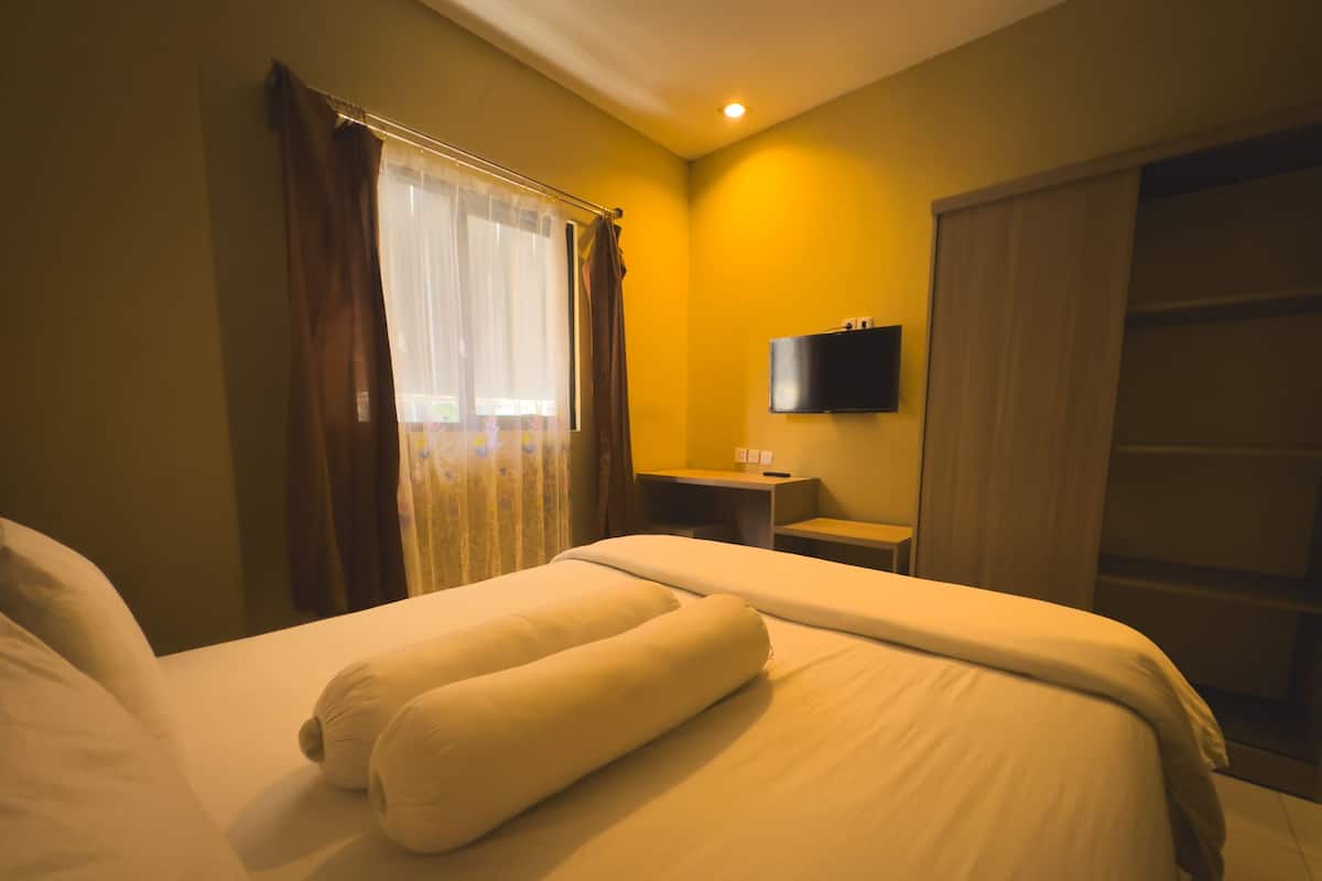 Hotellihuone, jossa on sänky, verhot, televisio ja työpöytä.
