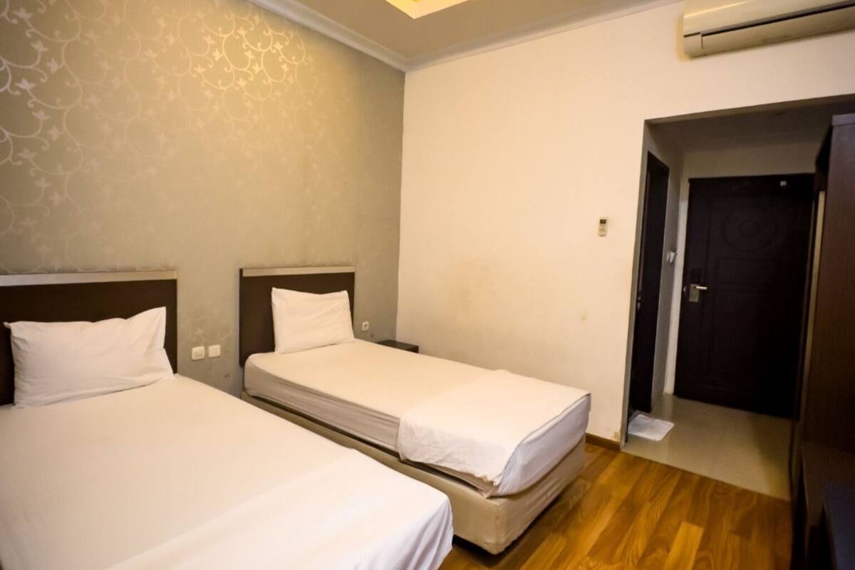 Hotellihuone, jossa on kaksi erillistä sänkyä, puulattia, kattovalaisin ja ilmastointilaite.