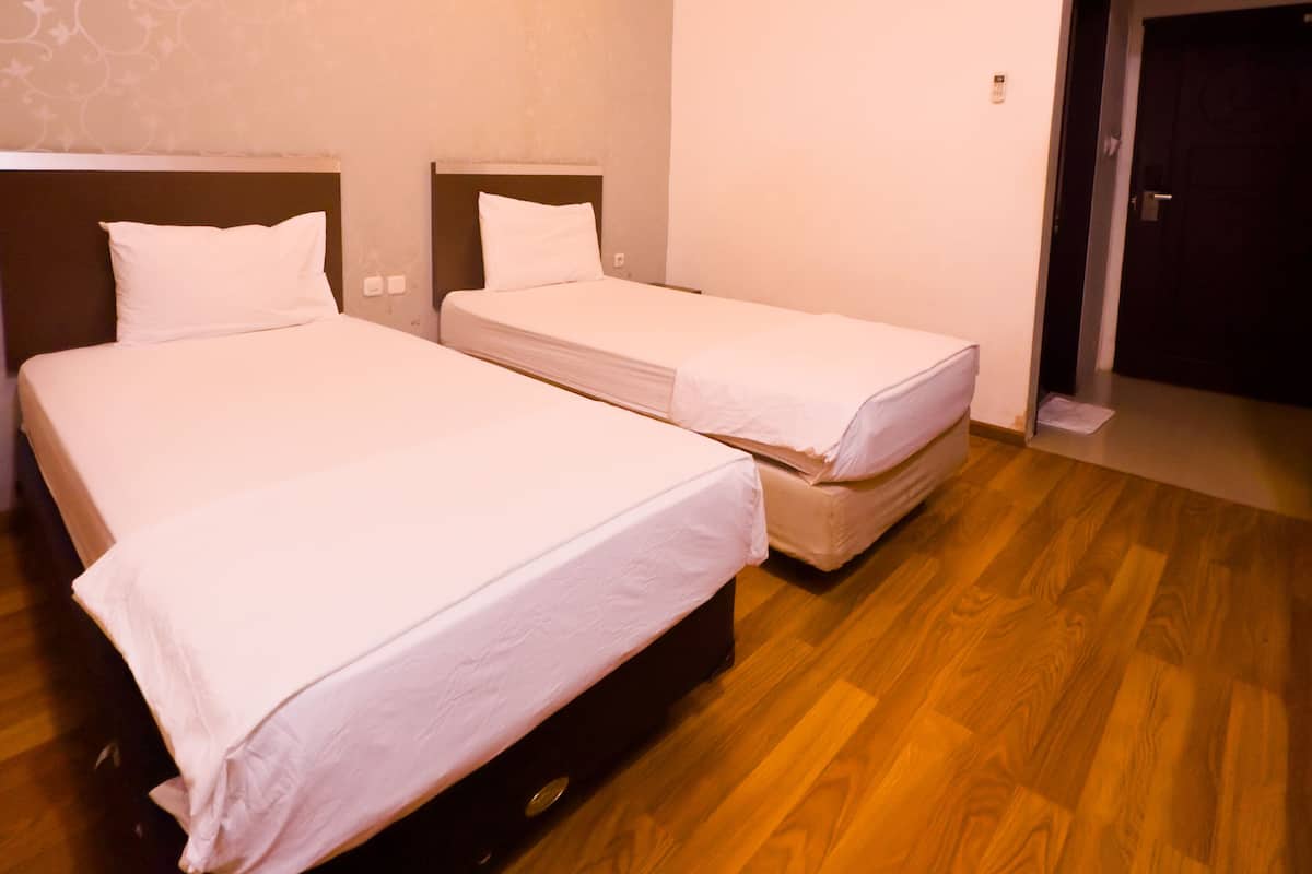 Hotellihuone, jossa on kaksi erillistä sänkyä, puulattia, kuvioitu seinä ja ilmastointilaite.