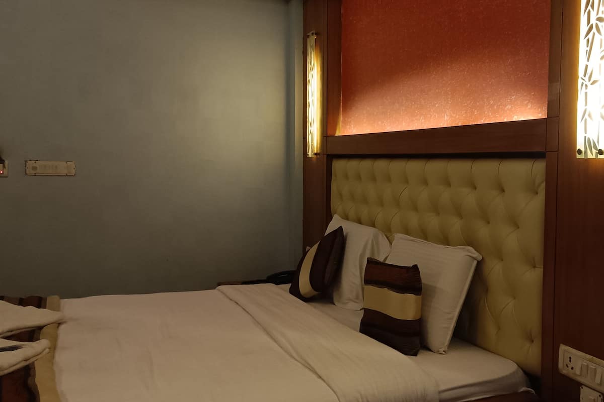 A hotel room with a large bed, a tufted headboard, and a wall-mounted light fixture.