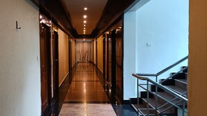 A hotel corridor with a polished floor, a staircase on the right, and doors on the left.