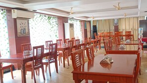 A dining area with multiple wooden tables and chairs, air conditioning units, and ceiling fans.