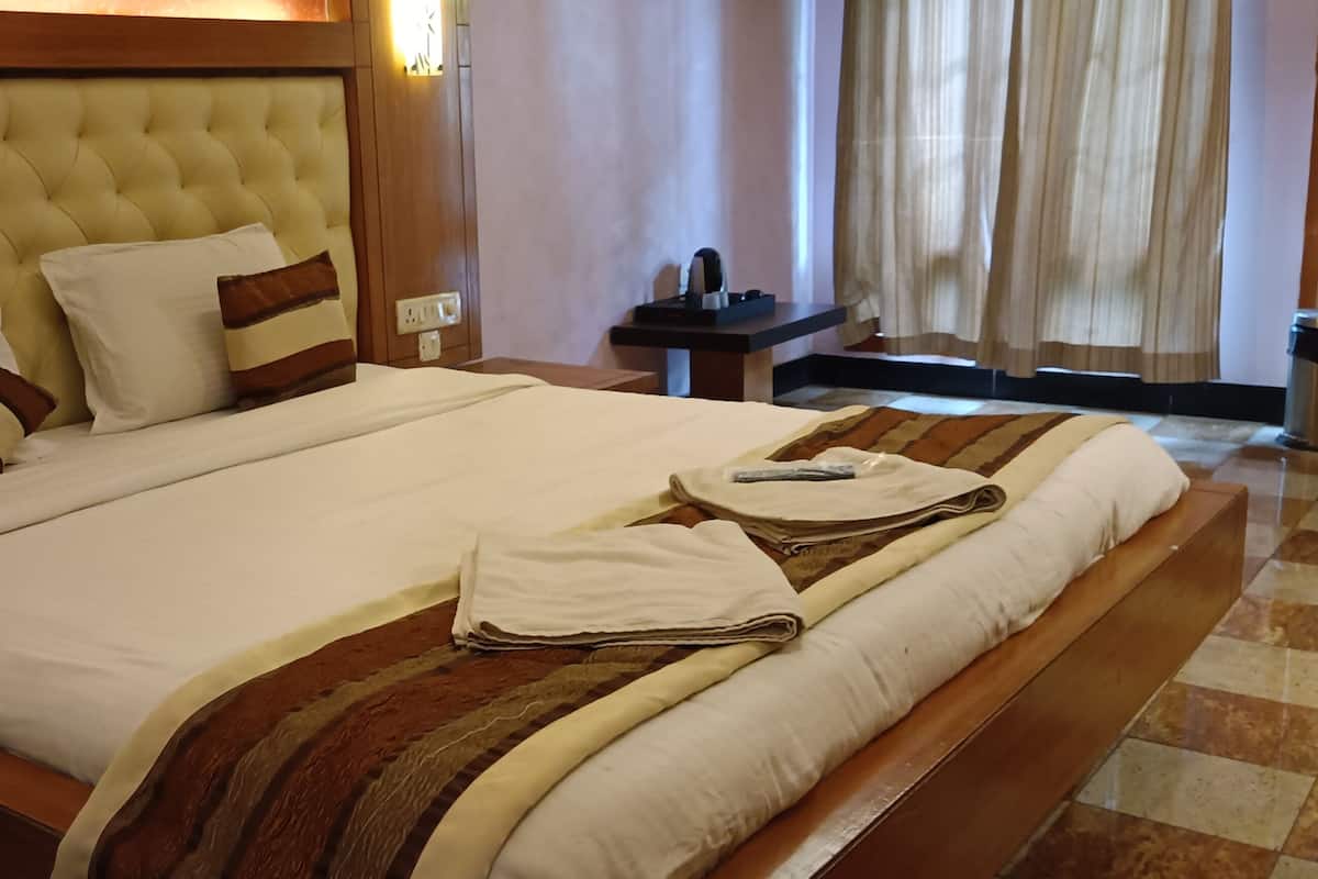 A hotel room with a large bed, a wooden headboard, a nightstand, a bedside table, and a window with curtains.