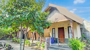A traditional house with a wooden door, a small porch, and a garden with various plants. - Hotel O Kost Gayus (Mataram)