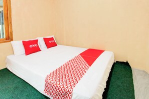 Una cama con ropa blanca y almohadas rojas, un plaid rojo y blanco, y alfombra verde.