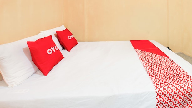 A bed with white bedding and two red pillows with a logo, a patterned red and white blanket, and a plain wall. - Hotel O Kost Gayus (Mataram)