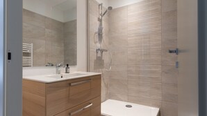 Ein modernes Badezimmer mit einem Holz-Waschtisch, einem großen Spiegel, einer Dusche mit Handbrause und einer Toilette.