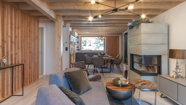 Ein modernes Wohnzimmer mit einer Couch, einem Couchtisch und einem Kamin. Ein Essbereich mit Stühlen und einem Fenster mit Blick auf eine Straße.