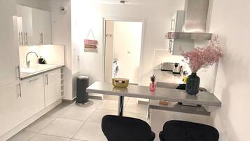 Una cocina moderna con armarios blancos, una campana extractora de acero inoxidable, un lavamanos y un comedor con dos sillas negras.