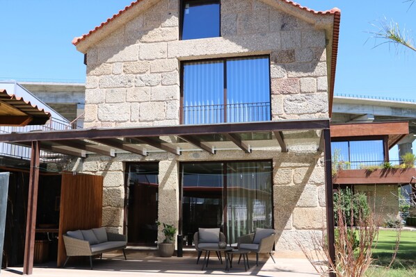 Ein Steinhaus mit überdachter Terrasse, Sitzgelegenheiten im Freien und Blick auf die Umgebung.
