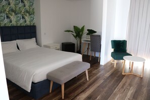 Ein modernes Hotelzimmer mit einem großen Bett, einem kleinen Schreibtisch, einem grünen Sessel und einem runden Tisch.
