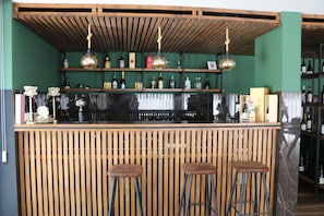 A bar area with wooden slats, three stools, and shelves with bottles and decorative items.