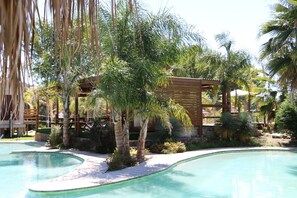 Ein Poolbereich mit einer Holzpergola, Palmen und einem klaren, blauen Pool.