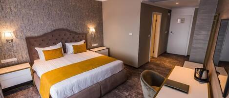 A modern hotel room with a large bed, two bedside tables, a desk with a chair, and a mirror.