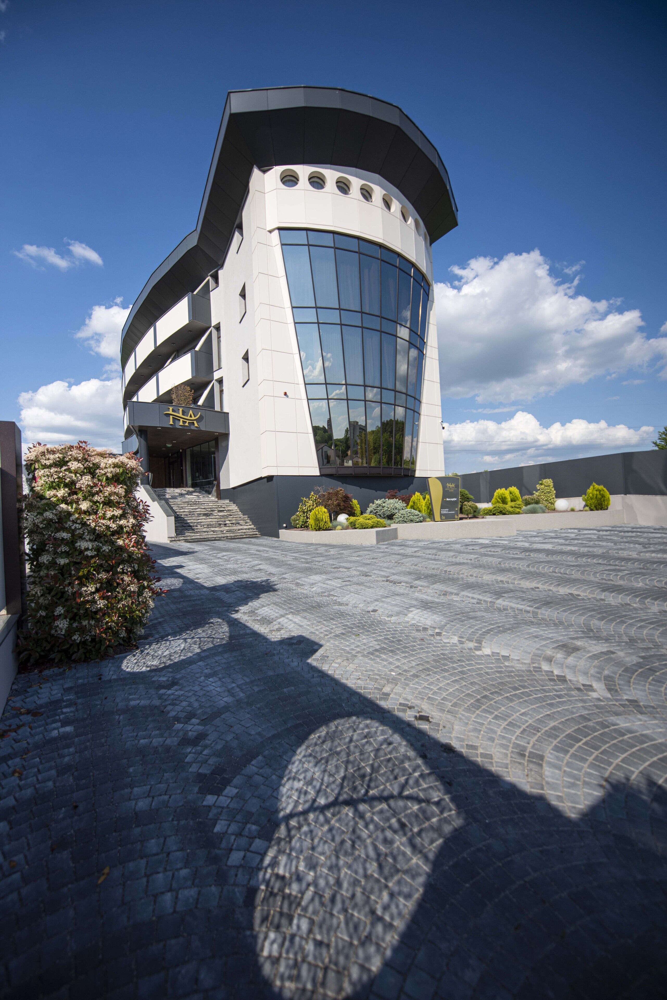 A modern building with a curved facade, large windows, and a paved entrance area with landscaping.
