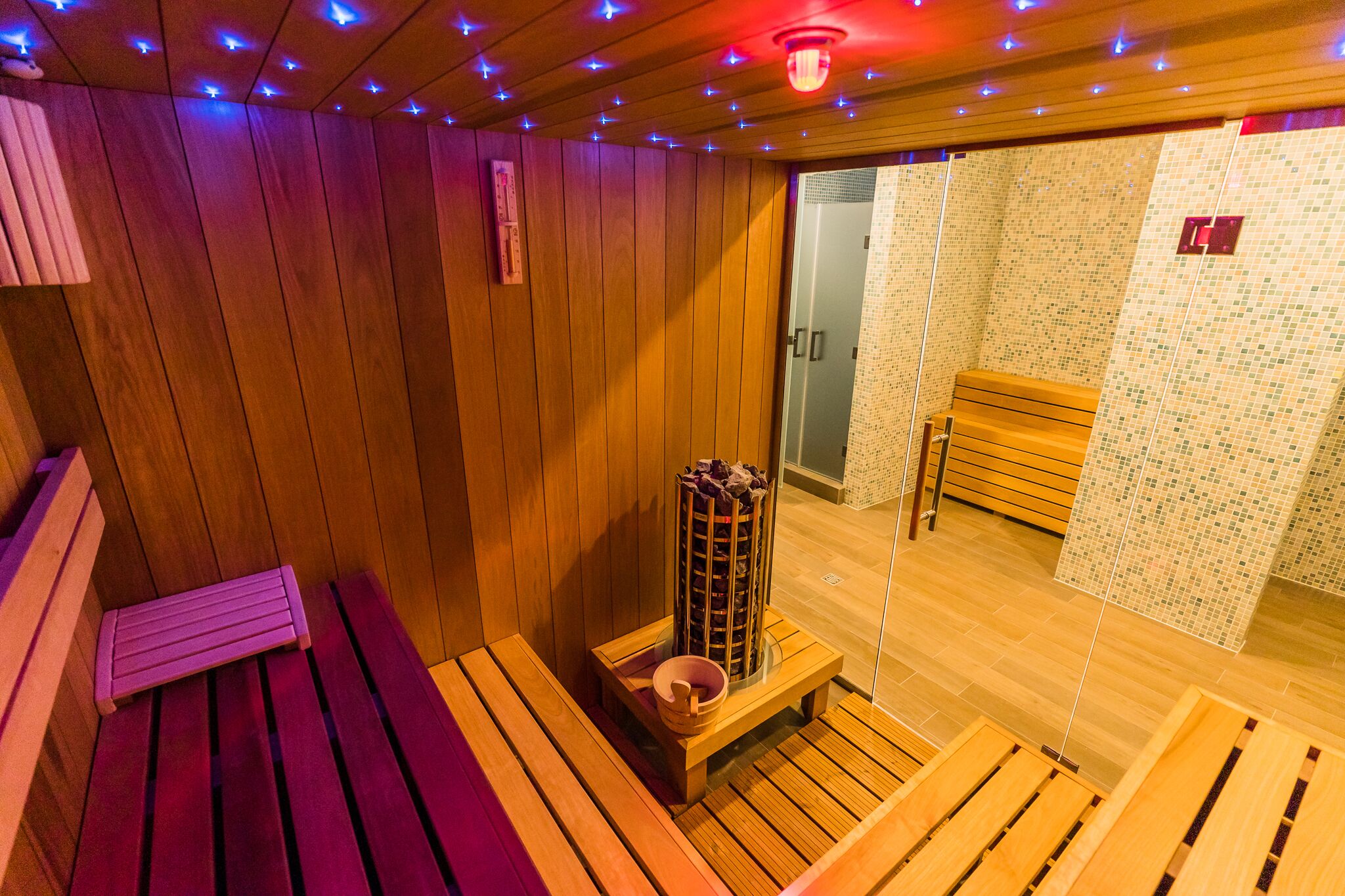 A wooden sauna with benches, a central heating column, and a tiled wall.