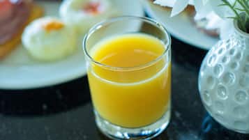 A breakfast table with plates of food, a glass of orange juice, and a white vase with a flower.