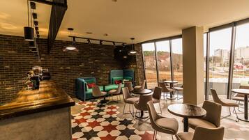 A modern cafe with a brick wall, green seating, and large windows offering a city view.