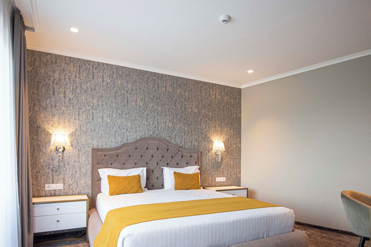 A modern hotel room with a large bed, two bedside tables, and a chair.