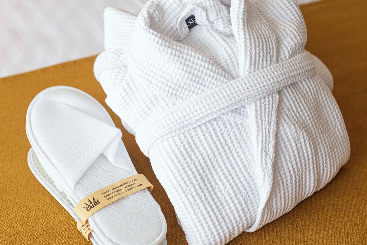 A neatly folded white bathrobe and a pair of white slippers on a mustard-colored bedspread.