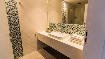 A modern bathroom with a white sink, a glass shower enclosure, and a tiled wall with a geometric pattern.