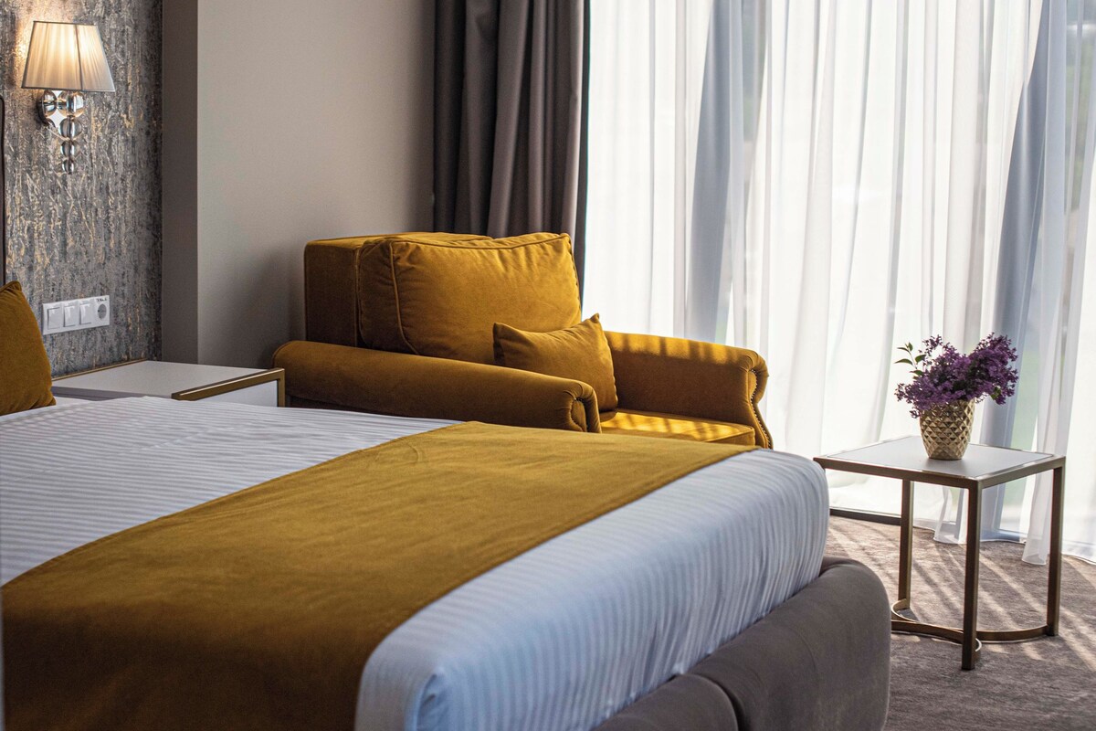 A hotel room with a large bed, a nightstand, a lamp, and a window with curtains.