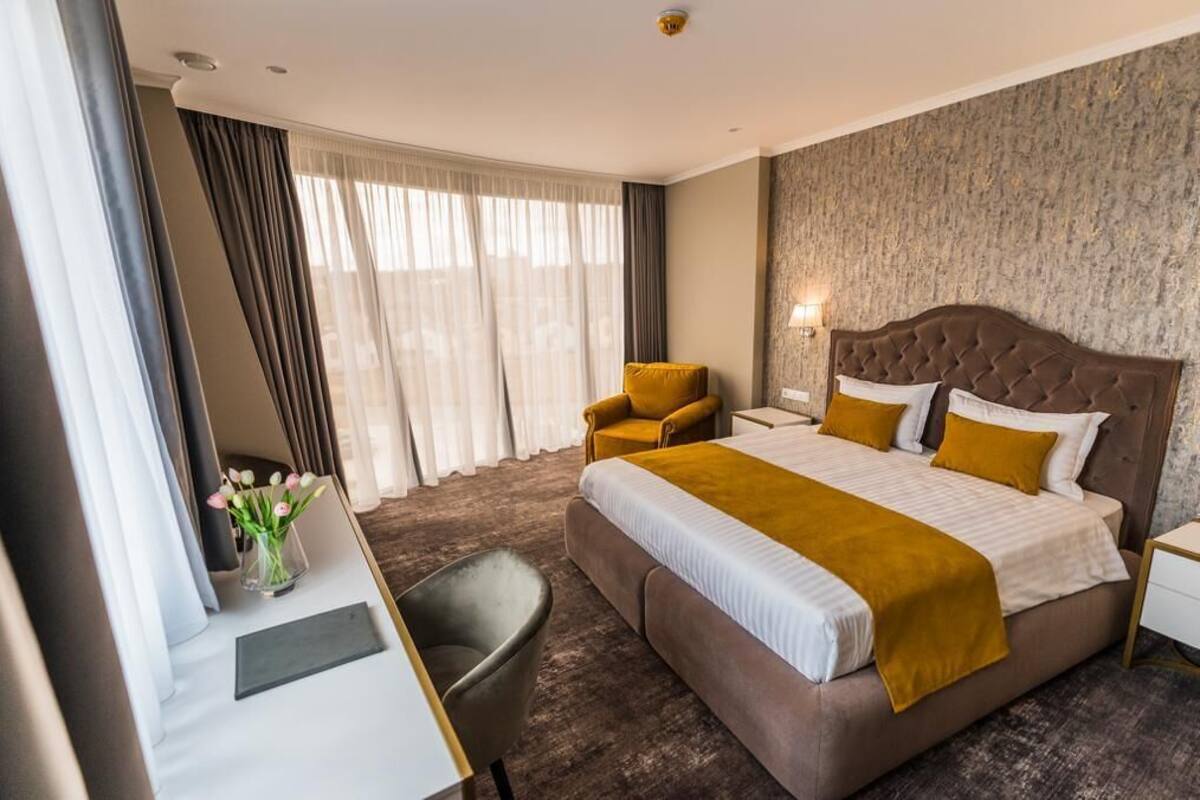 Une chambre d’hôtel avec un grand lit, un bureau avec une chaise, une petite table et un vase de fleurs.
