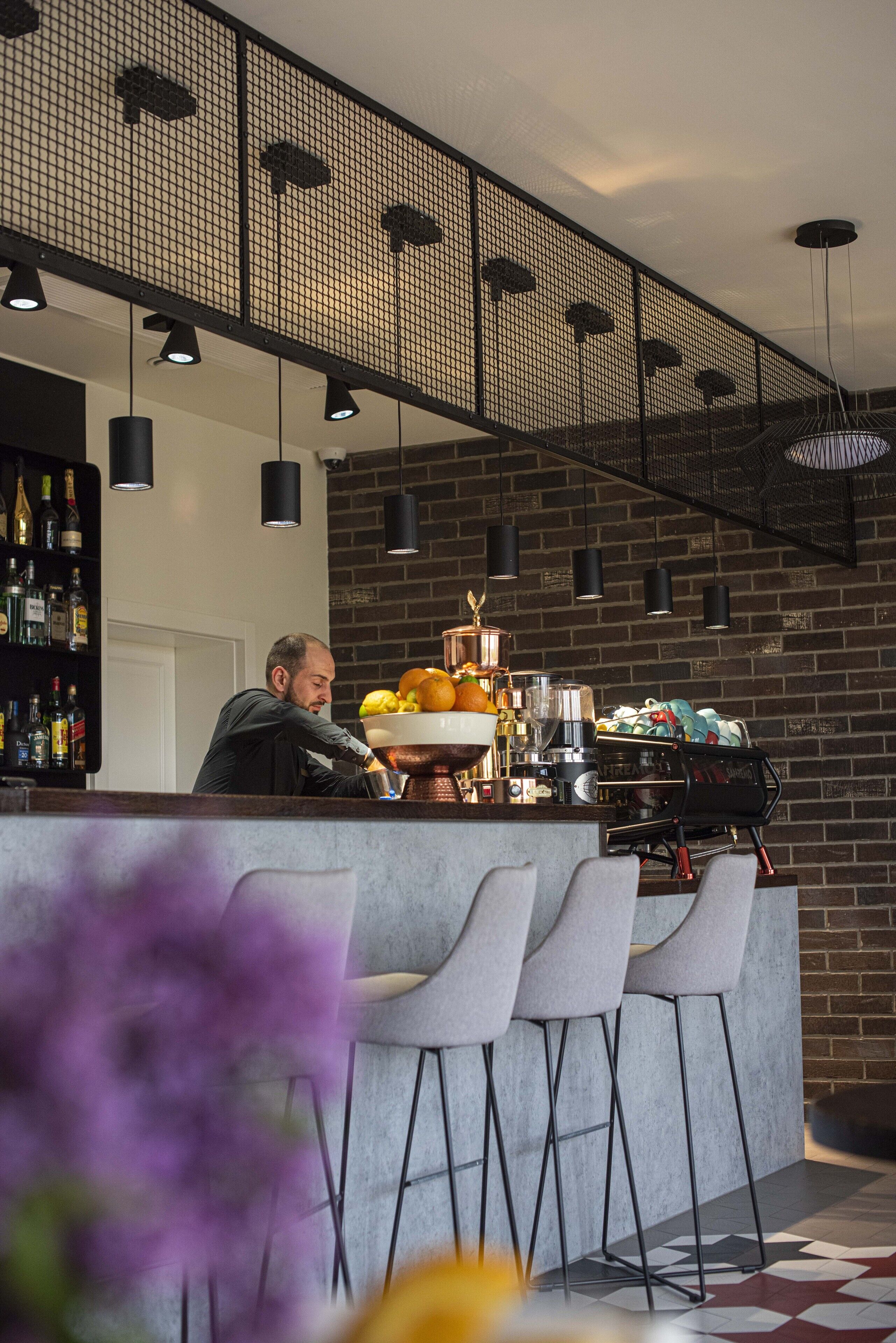 Un espace bar avec un barman, une machine à café et un assortiment de bouteilles exposées sur des étagères.