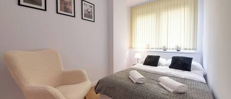 A bedroom with a bed, a chair, and three framed pictures on the wall.