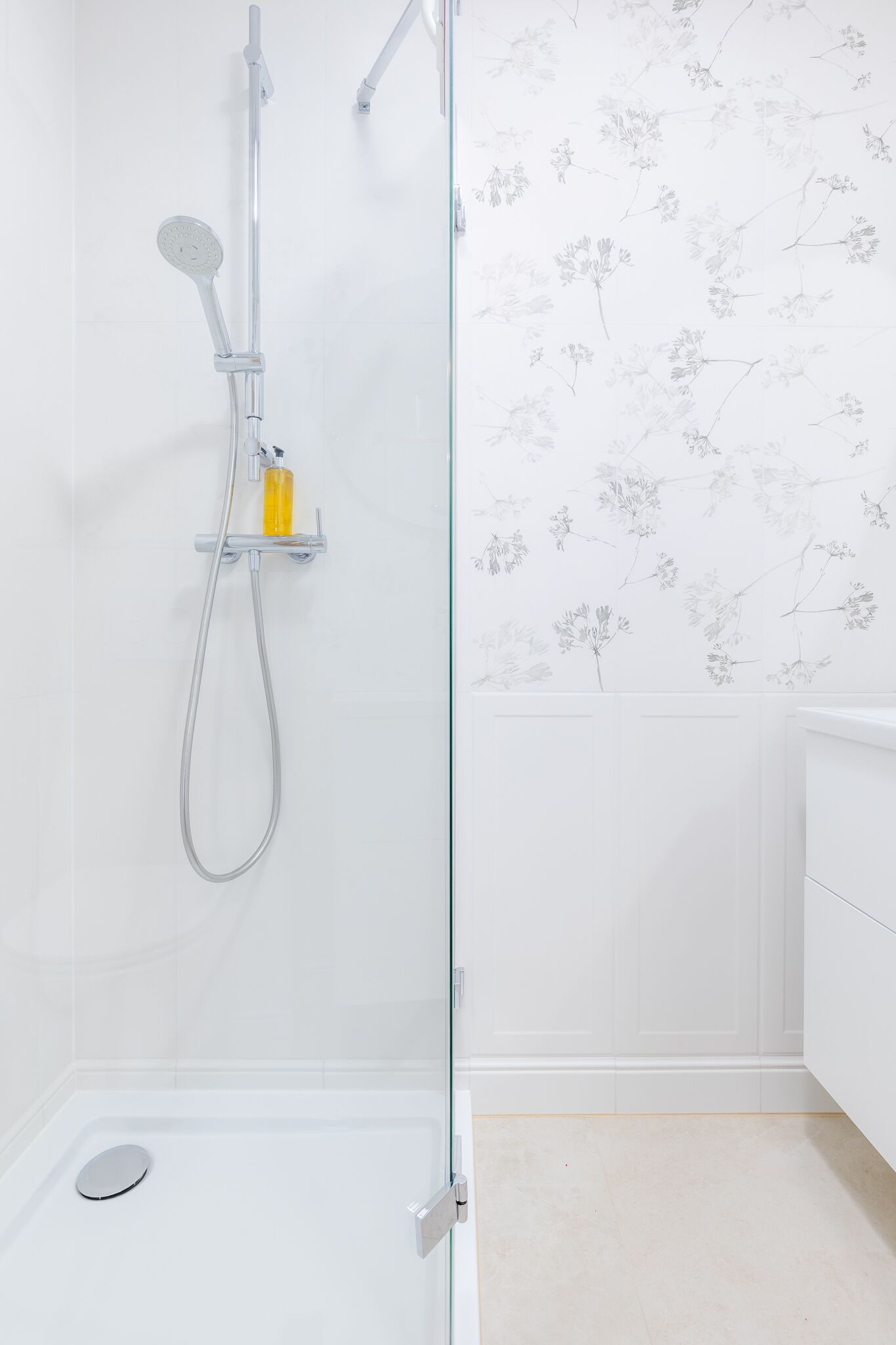 Ein modernes Badezimmer mit Duschkabine aus Glas, weiß gefliester Wand und floralem Wandpapier.