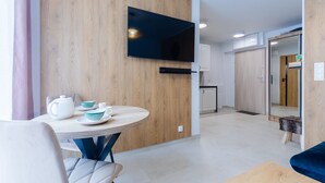 Un salon moderne avec une table ronde en bois, un téléviseur à écran plat fixé à un mur en bois, et un coin salon confortable avec un canapé bleu.