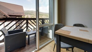 Un balcon avec une table et des chaises en bois, une porte vitrée et une vue sur un paysage montagneux.