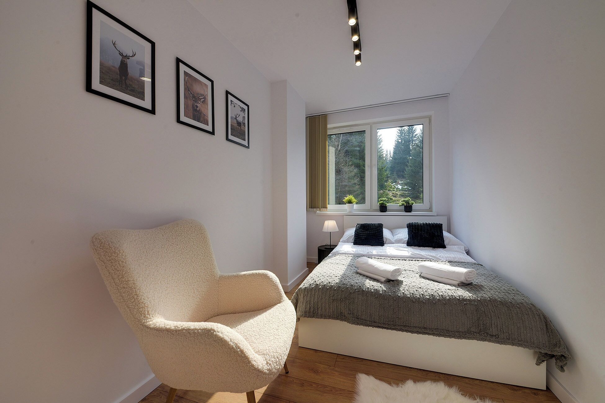 Une chambre à coucher avec un lit, une chaise, une fenêtre avec des plantes et des tableaux encadrés accrochés au mur.