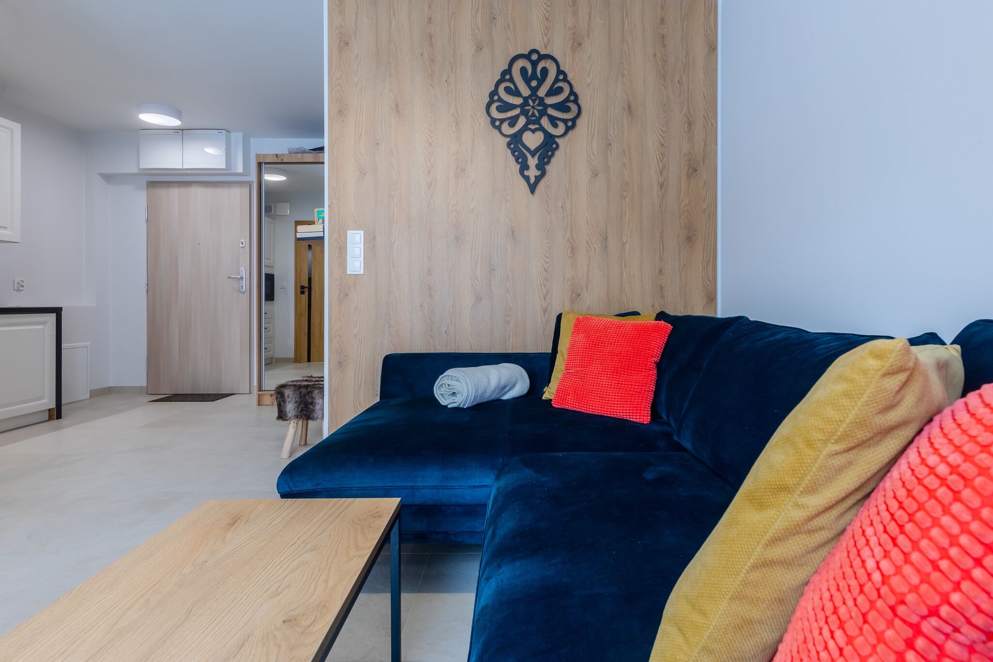 A modern living room with a dark blue sofa, a wooden accent wall, and a small wooden table.