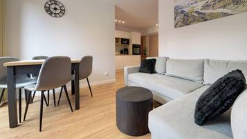 A modern living room with a grey sofa, a dining table with chairs, a round coffee table, and a kitchen in the background.