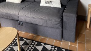 A grey sofa with two pillows, one with text, and a small wooden side table. - Domaine Au Bon, La Sud - 5min D'hossegor (Angresse)