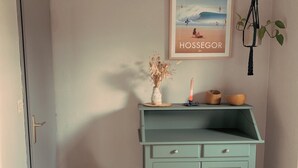 A room with a teal cabinet, a pink chair, a framed picture on the wall, and a hanging plant. - Domaine Au Bon, La Sud - 5min D'hossegor (Angresse)