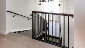 A staircase with a wooden ceiling, a black metal railing, and a hanging light fixture.