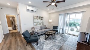 A spacious living room with a grey sofa, two armchairs, a coffee table, and a ceiling fan.