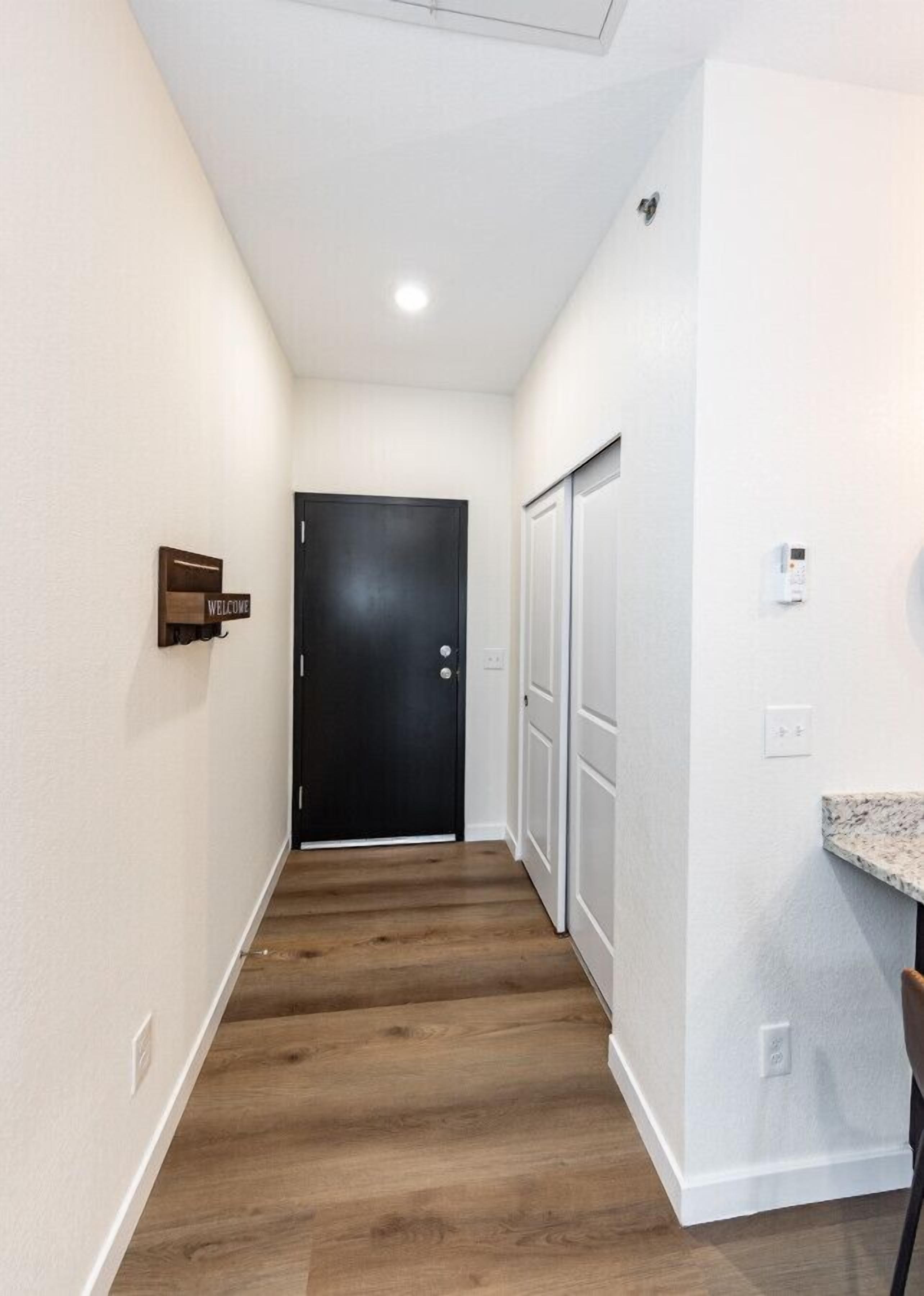 Un couloir étroit au plancher en bois, une porte noire au fond et un panneau d’accueil sur le mur de gauche.