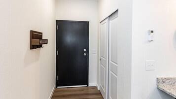 Un couloir étroit au plancher en bois, une porte noire au fond et un panneau d’accueil sur le mur de gauche.