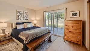 A bedroom with a bed, bedside tables, a bench, a wooden dresser, and a sliding glass door leading to an outdoor area. - 2 Bedroom Townhome with Private Garage!! (Frisco)